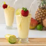 Pineapple, Coconut and Lime Blended in Tall Glass with a tray of fresh summer fruit