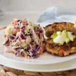 Two healthy tuna burgers on a white plate with honey Dijon coleslaw