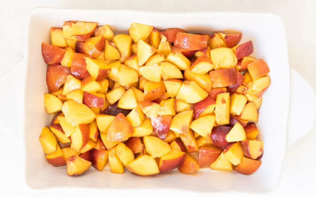 Large white baking pan filled with fresh cut peaches