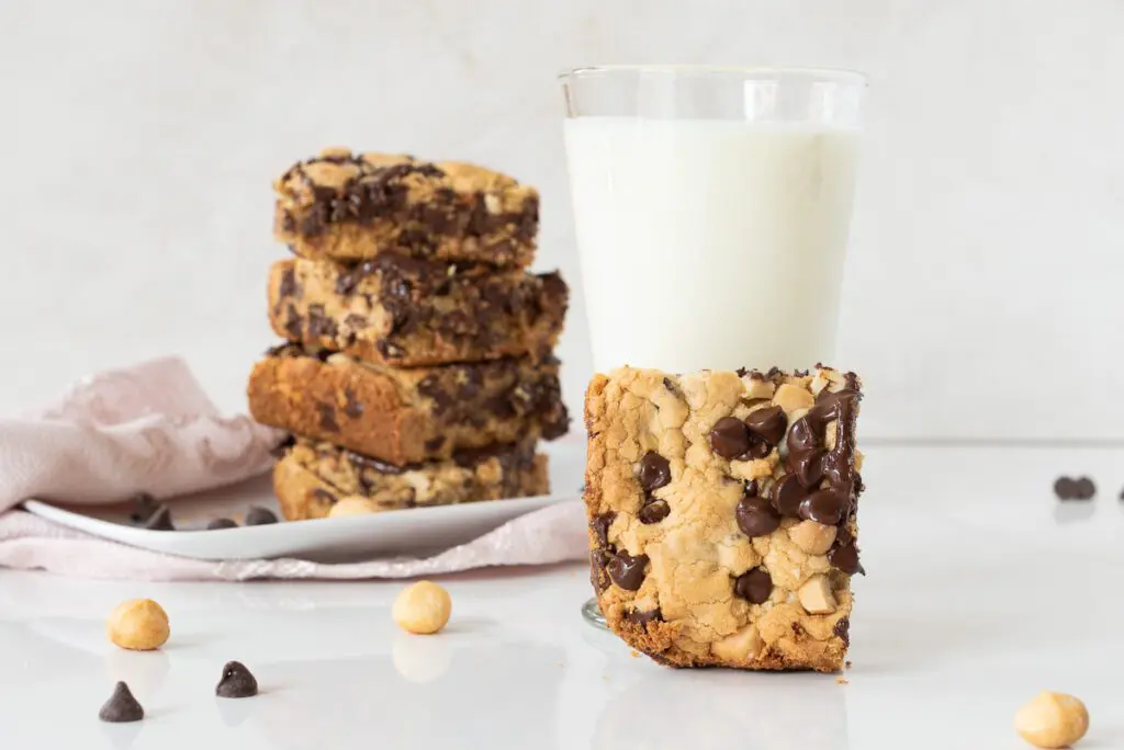 Stavk of gluten-free chocolate chip bar, a glass of milk and a hand holding a chocolate chip bar