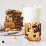 Stavk of gluten-free chocolate chip bar, a glass of milk and a hand holding a chocolate chip bar