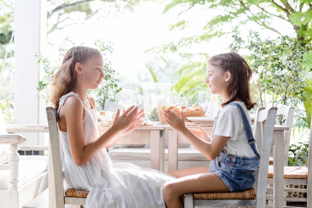 Two girls sitting at a table in the sunshine
