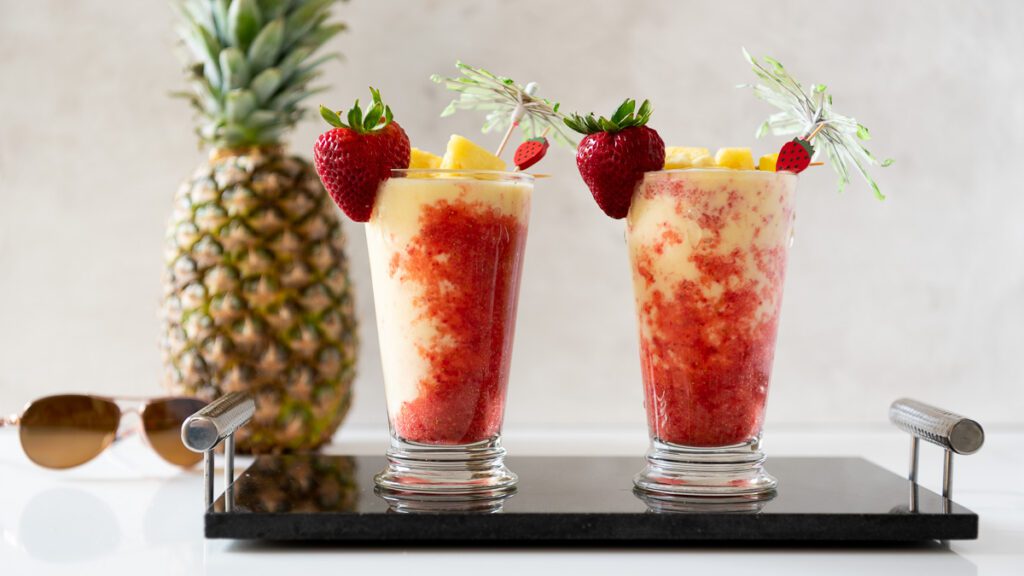 Pina Colada and Strawberry Puree in a tall glass with umbrellas 