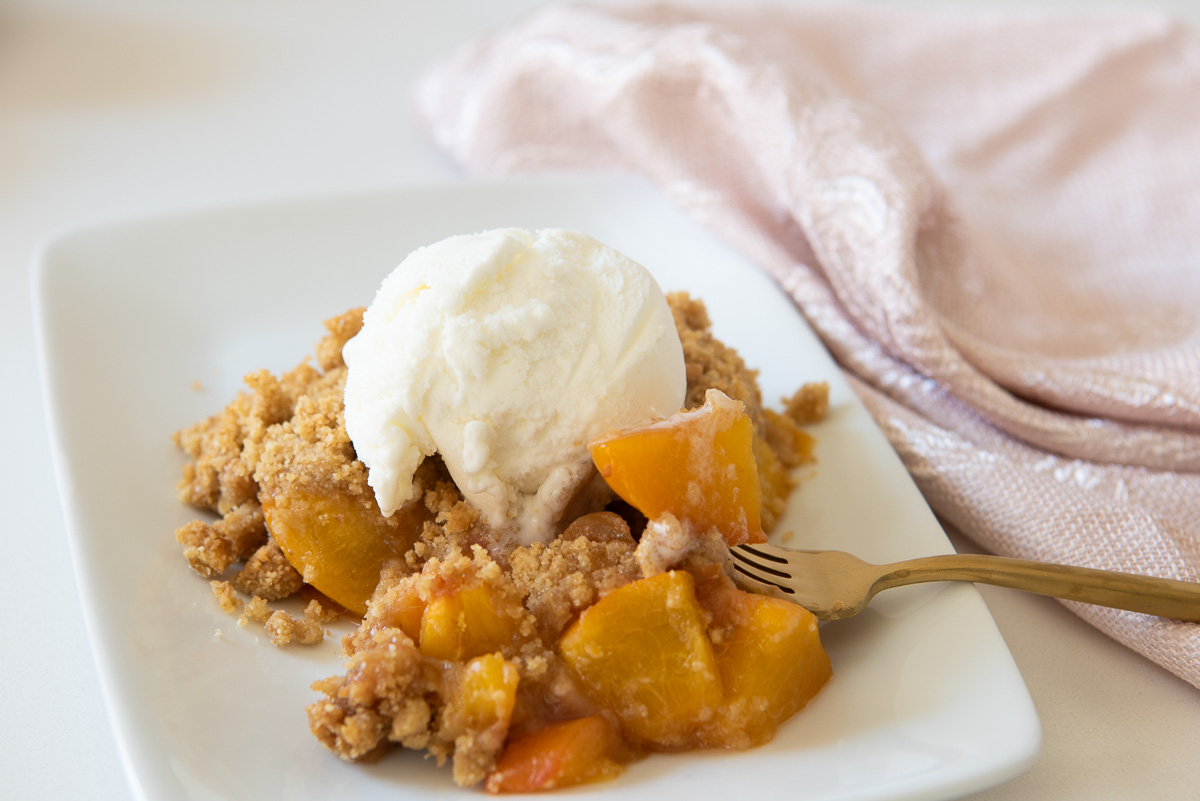 GF Peach Cobbler with Ice Cream on a White Plate with a Gold Fork and a Pink Napkin