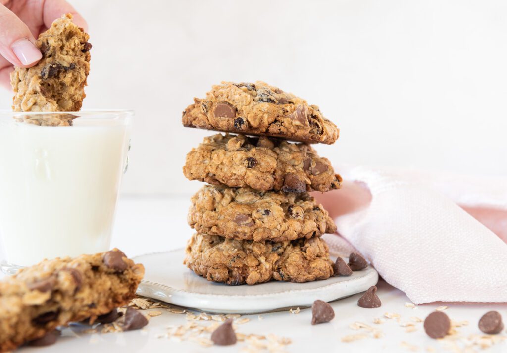 Dunking a Oatmeal Cookie in Milk with a stack of cookies nearby 