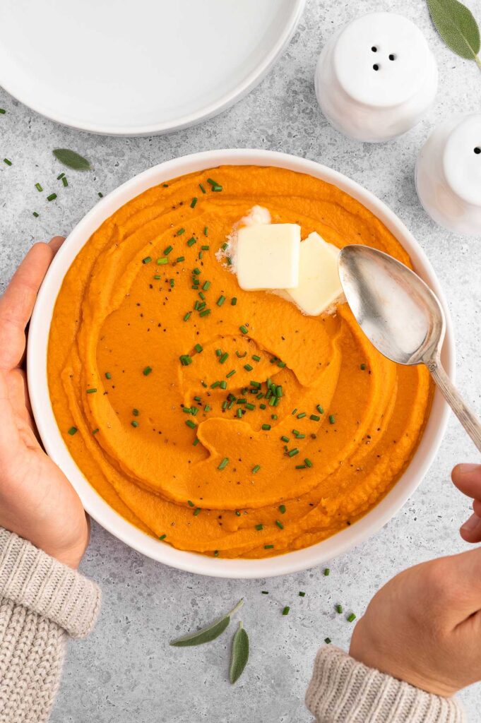 Hands holding a large bowl of mashed sweet potatoes 