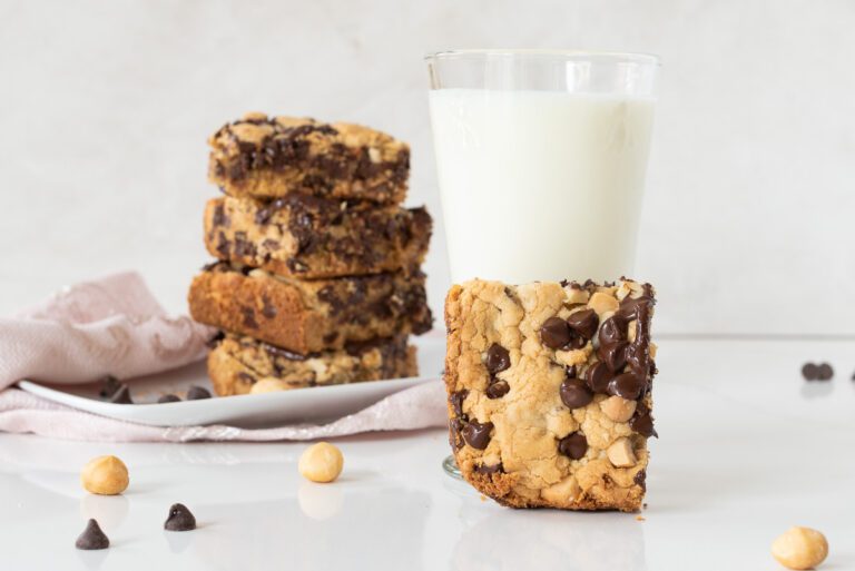 Stavk of gluten-free chocolate chip bar, a glass of milk and a hand holding a chocolate chip bar