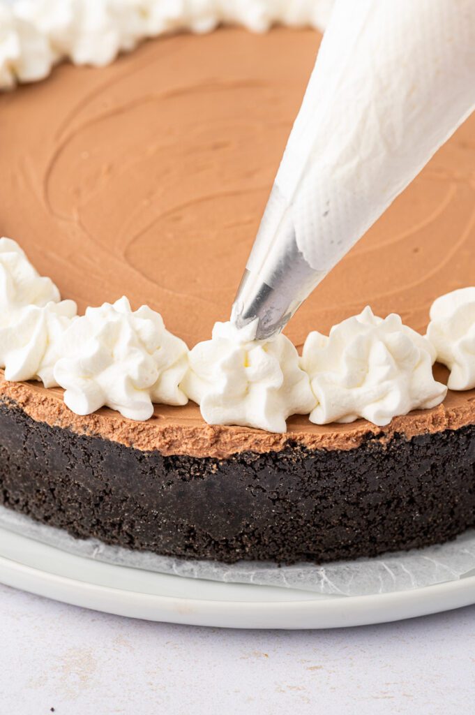Piping whipped cream on top of chocolate cheesecake 